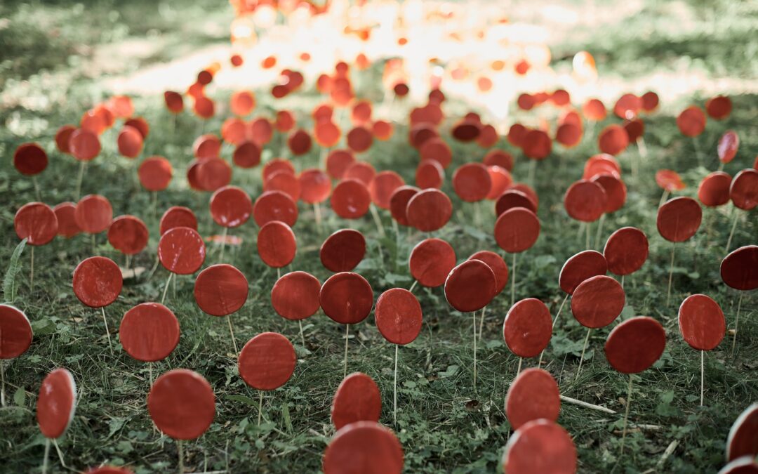 Red lollipops on stick against green grass, outdoor land art objects for environmental concept